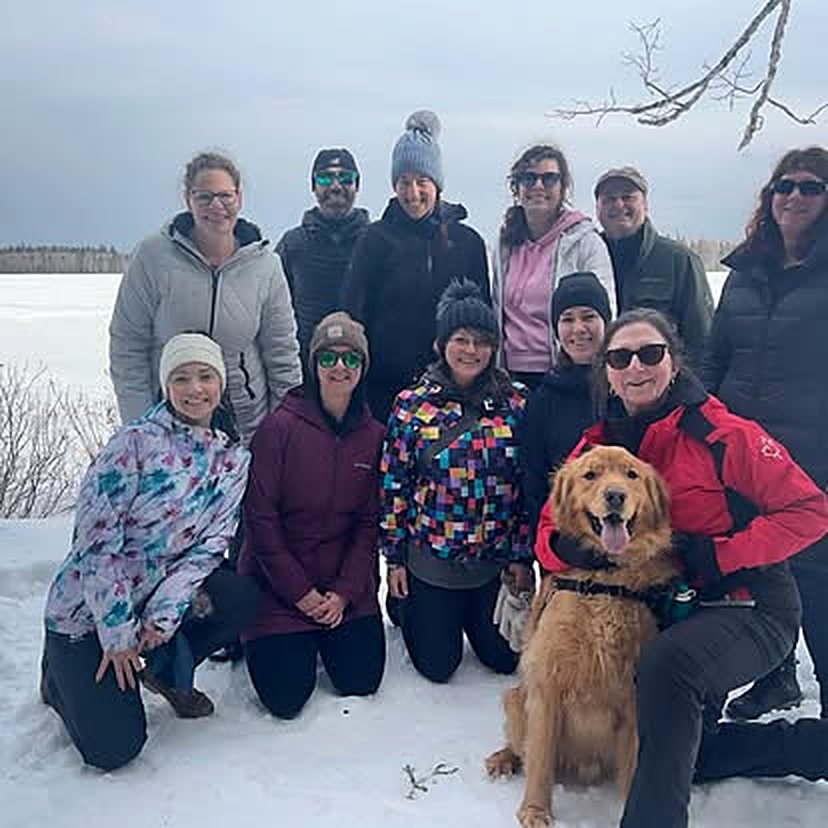 A group of Premium Fitness members smiling together outdoors in the snow with a golden retriever